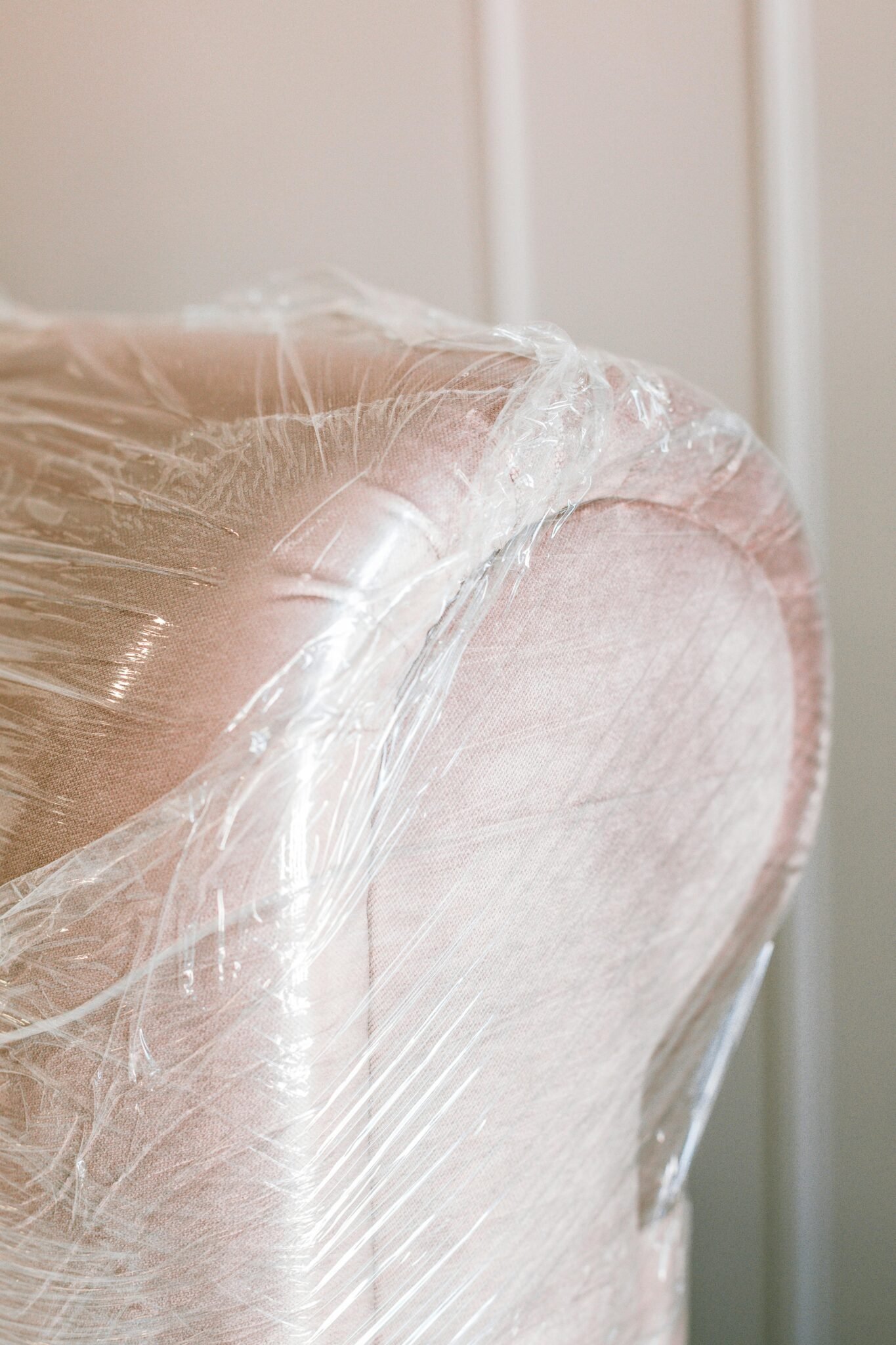 Close-up of a pink armchair covered in protective plastic wrap for moving.